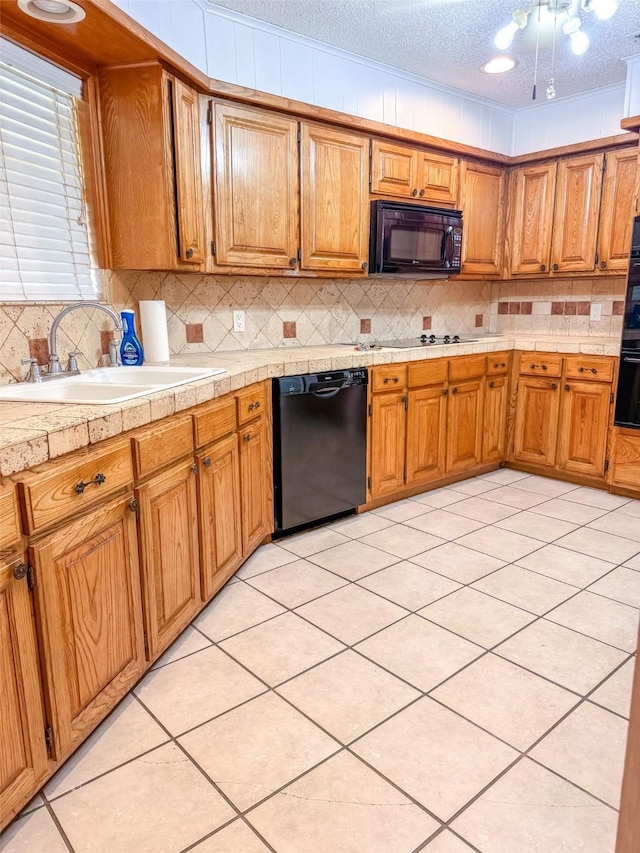 kitchen with a textured ceiling, a sink, light countertops, black appliances, and brown cabinetry