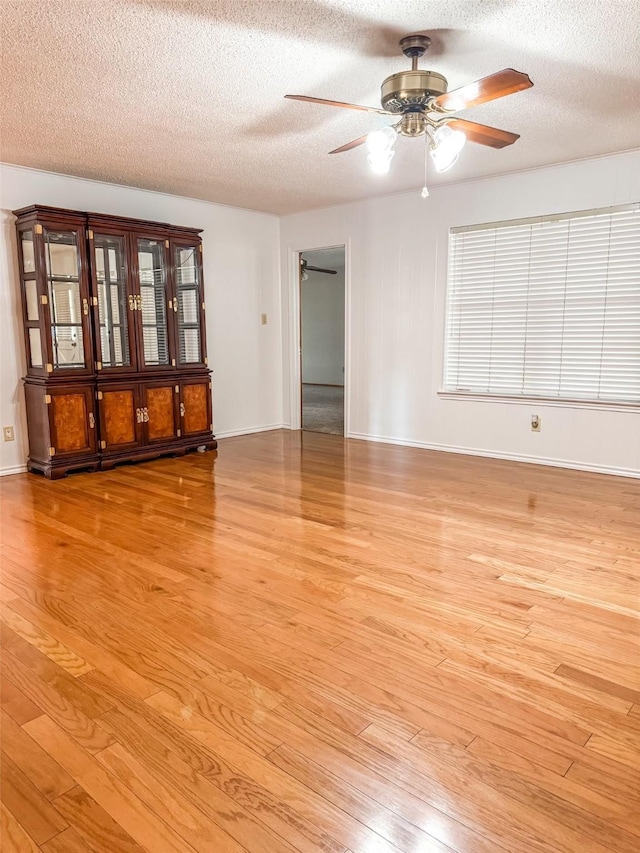 empty room featuring a textured ceiling, ceiling fan, baseboards, and light wood-style floors