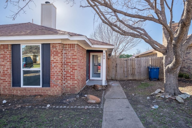 view of side of home featuring roof with shingles, a chimney, fence, and brick siding