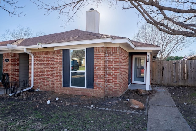 exterior space featuring roof with shingles, brick siding, a chimney, and fence