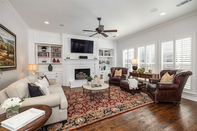 living area with dark wood-type flooring, a fireplace, visible vents, and crown molding