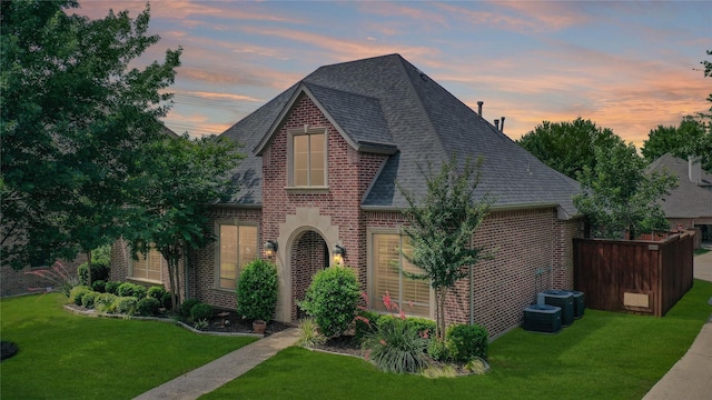 view of front of property with brick siding, a shingled roof, and a yard