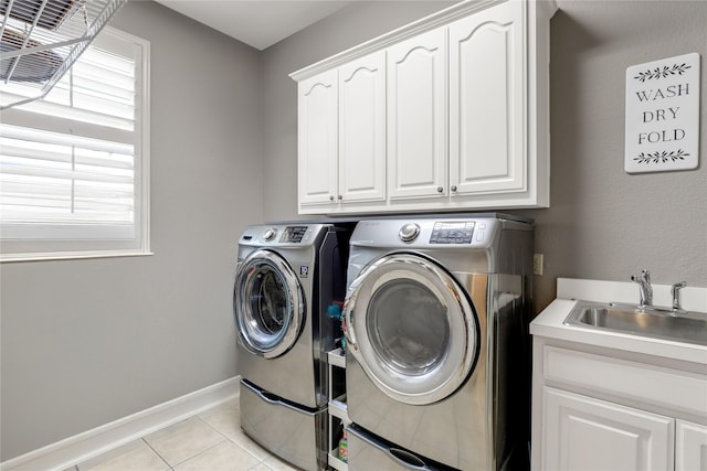 laundry area with light tile patterned floors, cabinet space, washing machine and dryer, a sink, and baseboards