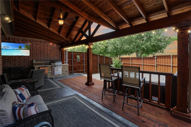 wooden deck featuring an outdoor kitchen, ceiling fan, fence, a gazebo, and outdoor dining space