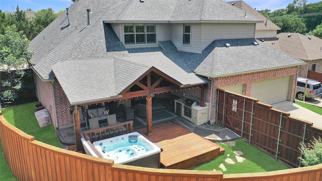 rear view of house with a garage, brick siding, roof with shingles, and hot tub deck surround