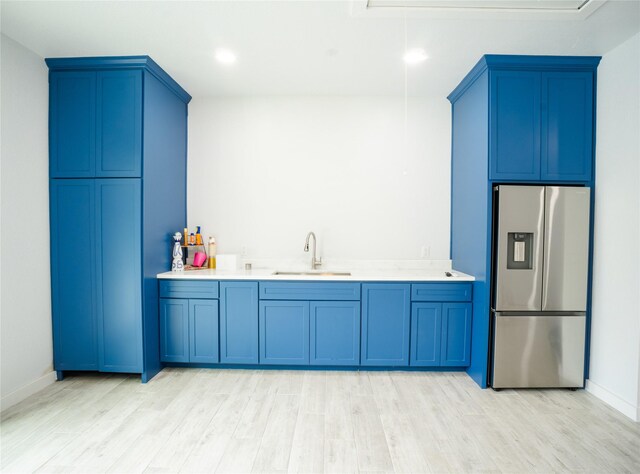 kitchen featuring blue cabinets, stainless steel refrigerator with ice dispenser, a sink, and light countertops