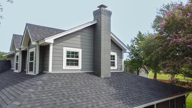 view of side of home with roof with shingles and a chimney