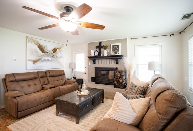 living room featuring a ceiling fan, a large fireplace, visible vents, and plenty of natural light