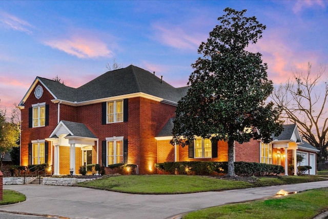 view of front of home with brick siding, a lawn, driveway, and a shingled roof