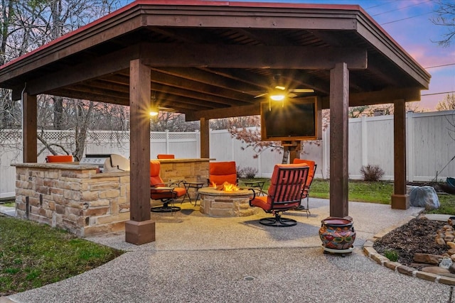 view of patio / terrace with a fenced backyard, an outdoor fire pit, a gazebo, and exterior kitchen