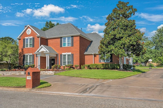 view of front of home featuring brick siding, a front yard, driveway, and a shingled roof