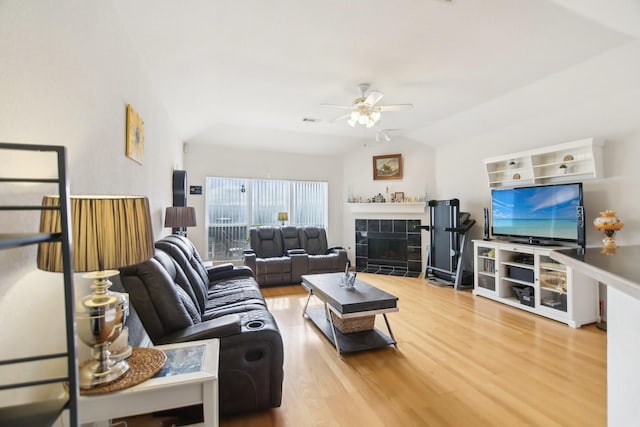 living area with lofted ceiling, wood finished floors, ceiling fan, and a tile fireplace