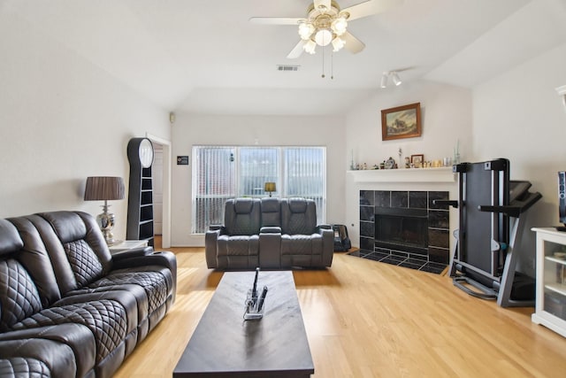 living room with lofted ceiling, a tiled fireplace, wood finished floors, and visible vents