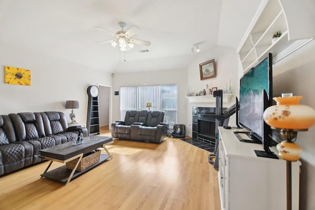 living room with light wood-type flooring, a fireplace, visible vents, and a ceiling fan