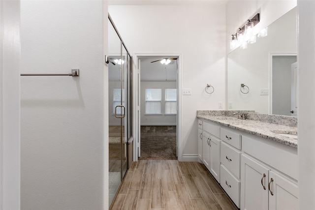 bathroom featuring double vanity, wood finish floors, a stall shower, and baseboards