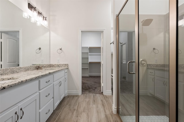 full bath featuring double vanity, a spacious closet, a sink, a shower stall, and wood finished floors