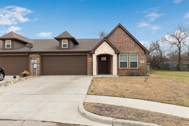 view of front facade featuring brick siding, a front yard, a garage, stone siding, and driveway