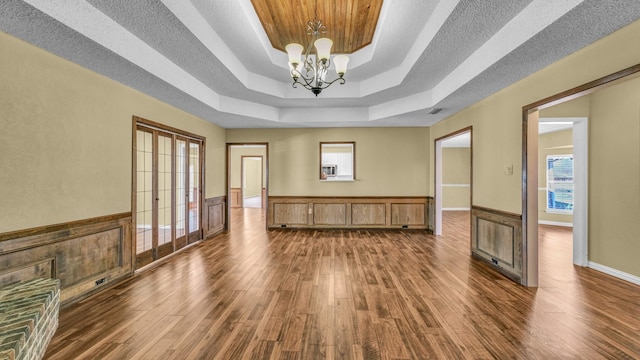 empty room with a raised ceiling, wainscoting, dark wood-style flooring, an inviting chandelier, and a textured ceiling