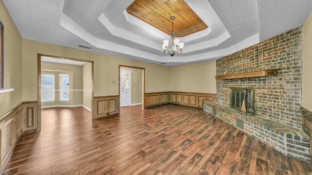 unfurnished living room featuring visible vents, a brick fireplace, a raised ceiling, dark wood finished floors, and an inviting chandelier