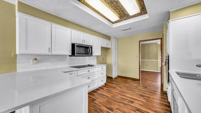 kitchen featuring white cabinets, dark wood finished floors, stainless steel microwave, black electric stovetop, and light countertops