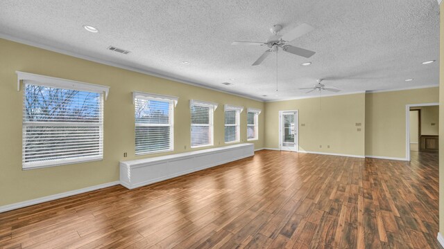 empty room featuring a textured ceiling, wood finished floors, visible vents, baseboards, and ornamental molding