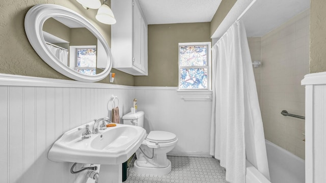 full bathroom featuring shower / tub combo with curtain, toilet, wainscoting, a sink, and tile patterned floors