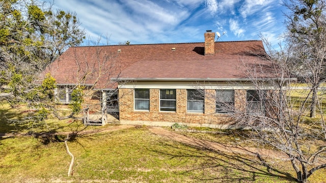 rear view of house with a shingled roof, a chimney, a lawn, and brick siding