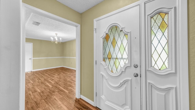 foyer entrance featuring a textured ceiling, a chandelier, wood finished floors, visible vents, and a healthy amount of sunlight