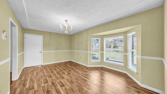 unfurnished room featuring a chandelier, a textured ceiling, wood finished floors, and baseboards