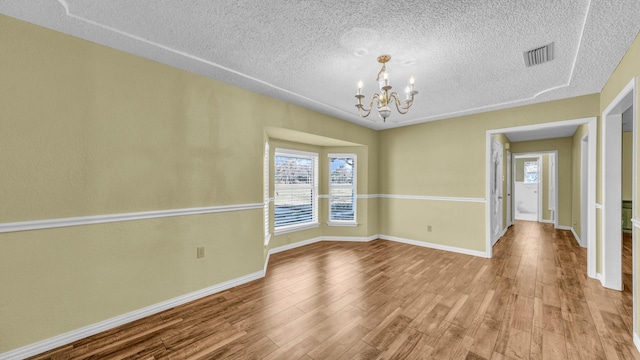 spare room featuring baseboards, visible vents, wood finished floors, a textured ceiling, and a notable chandelier