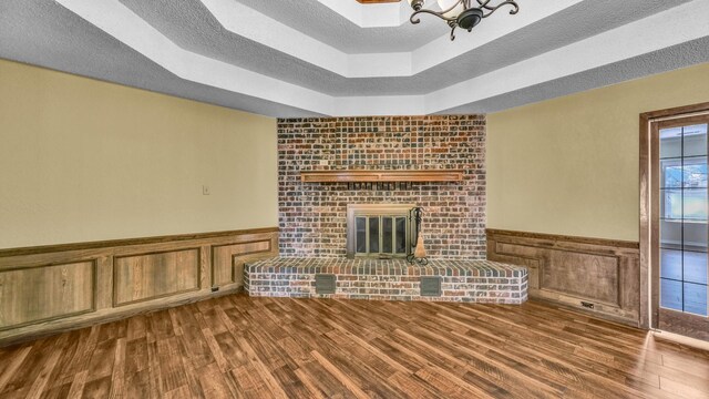 unfurnished living room with a wainscoted wall, a fireplace, a textured ceiling, and wood finished floors