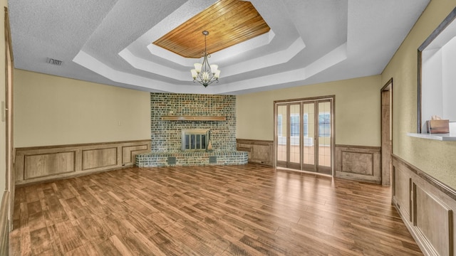 unfurnished living room featuring a tray ceiling, a wainscoted wall, visible vents, an inviting chandelier, and a brick fireplace