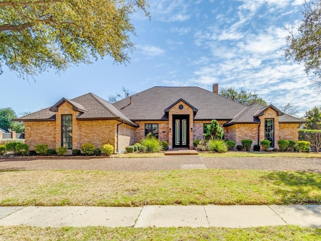 view of front of house featuring brick siding, a chimney, a shingled roof, and a front yard