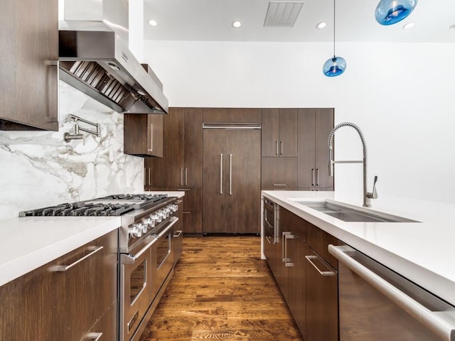 kitchen with light countertops, wall chimney range hood, premium appliances, and a sink