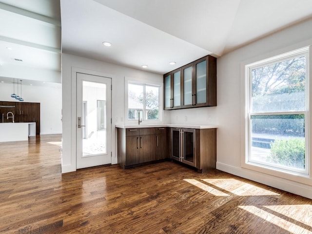 kitchen with baseboards, dark wood finished floors, light countertops, dark brown cabinetry, and glass insert cabinets