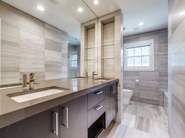 full bath with tile walls, double vanity, and a sink