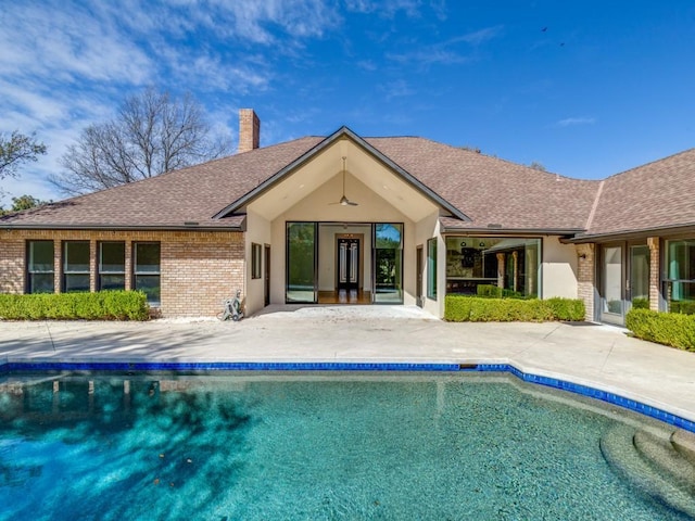 back of property featuring a ceiling fan, an outdoor pool, a chimney, a patio area, and brick siding