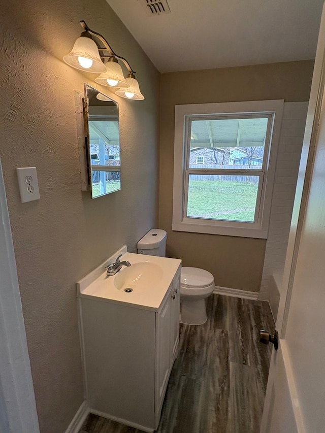 full bath featuring vanity, plenty of natural light, wood finished floors, and toilet