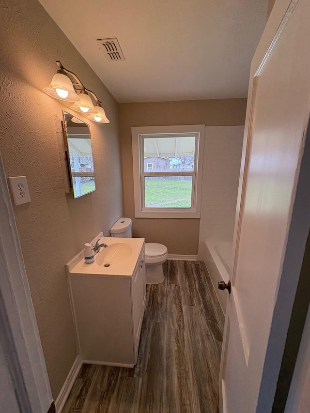 bathroom featuring visible vents, toilet, a bathing tub, vanity, and wood finished floors