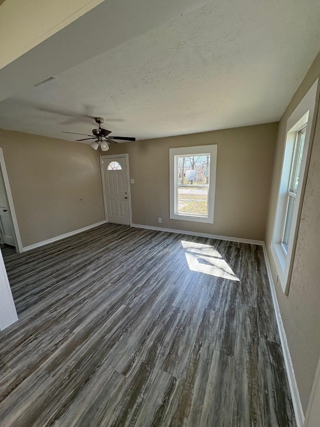 unfurnished living room featuring dark wood finished floors, a textured ceiling, baseboards, and ceiling fan