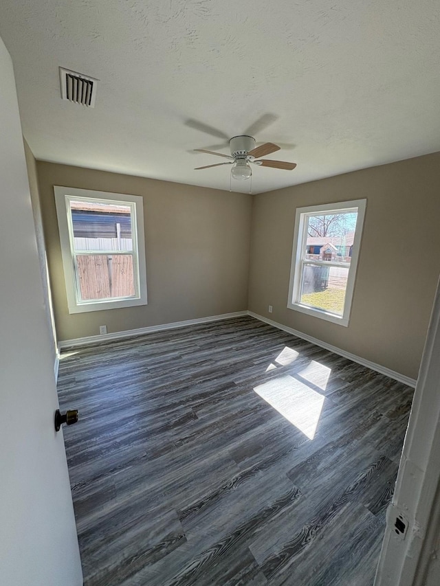 empty room featuring a textured ceiling, dark wood-type flooring, a ceiling fan, visible vents, and baseboards