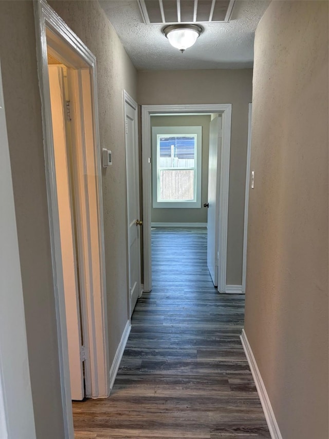 hallway with dark wood-type flooring, visible vents, a textured wall, and a textured ceiling