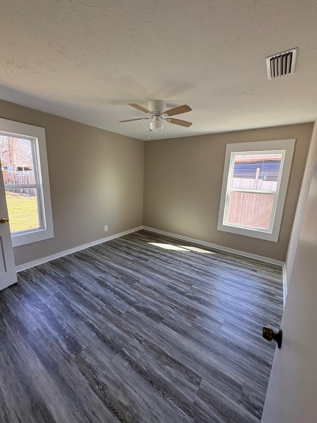 spare room featuring ceiling fan, a textured ceiling, visible vents, baseboards, and dark wood-style floors