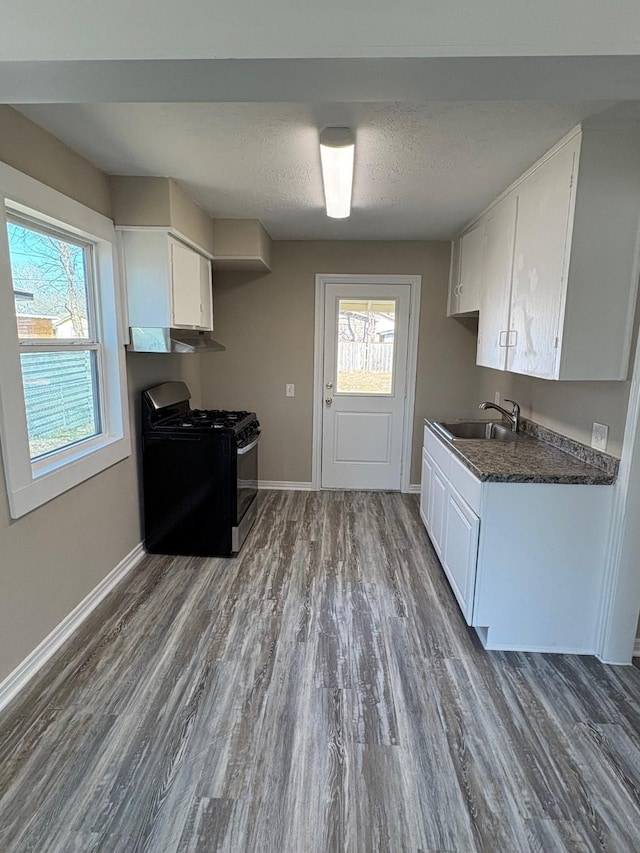 kitchen with stainless steel range with gas cooktop, dark countertops, a sink, under cabinet range hood, and baseboards