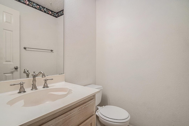 bathroom with a textured wall, vanity, and toilet