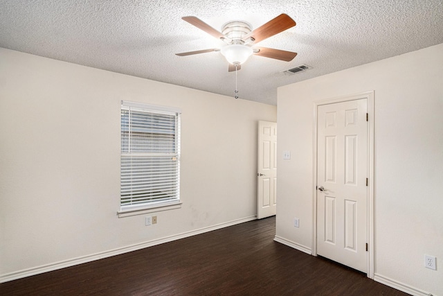 unfurnished room with a textured ceiling, visible vents, baseboards, a ceiling fan, and dark wood finished floors