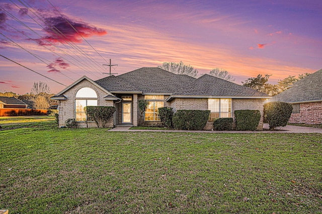 view of front of property with a shingled roof, a front yard, and brick siding