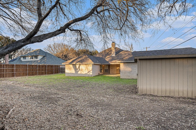 rear view of property featuring a yard, brick siding, a chimney, and fence