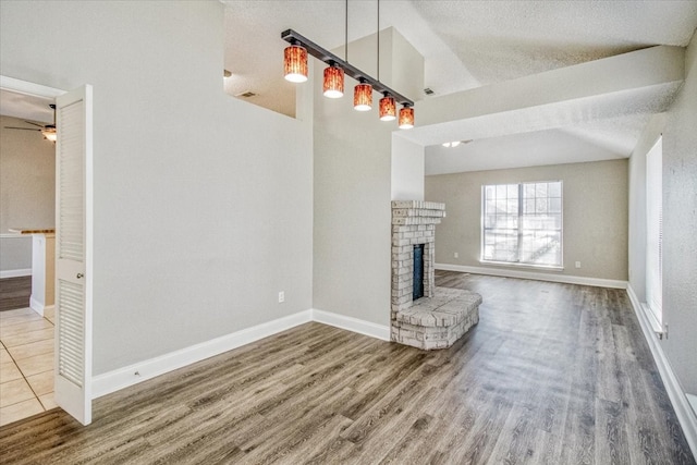 unfurnished living room featuring a brick fireplace, baseboards, visible vents, and wood finished floors