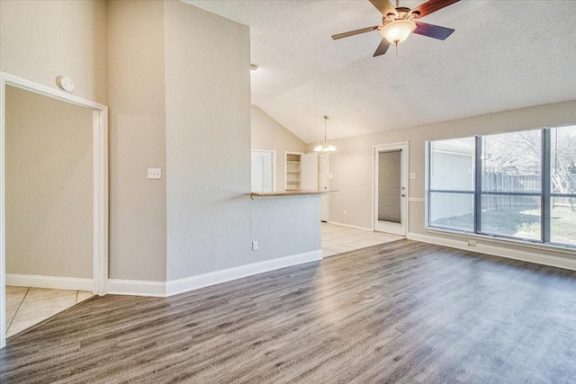 unfurnished living room with ceiling fan with notable chandelier, a textured ceiling, wood finished floors, and lofted ceiling